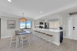 A modern kitchen with white cabinetry, a central island, and a dining area with white chairs. - Beachfront 2B/2B Sandarac Vacation Condo 506B. Direct gulf view! (Fort Myers Beach)