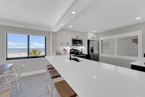 A modern kitchen with a large island, white cabinetry, and a view of the beach. - Beachfront 2B/2B Sandarac Vacation Condo 506B. Direct gulf view! (Fort Myers Beach)
