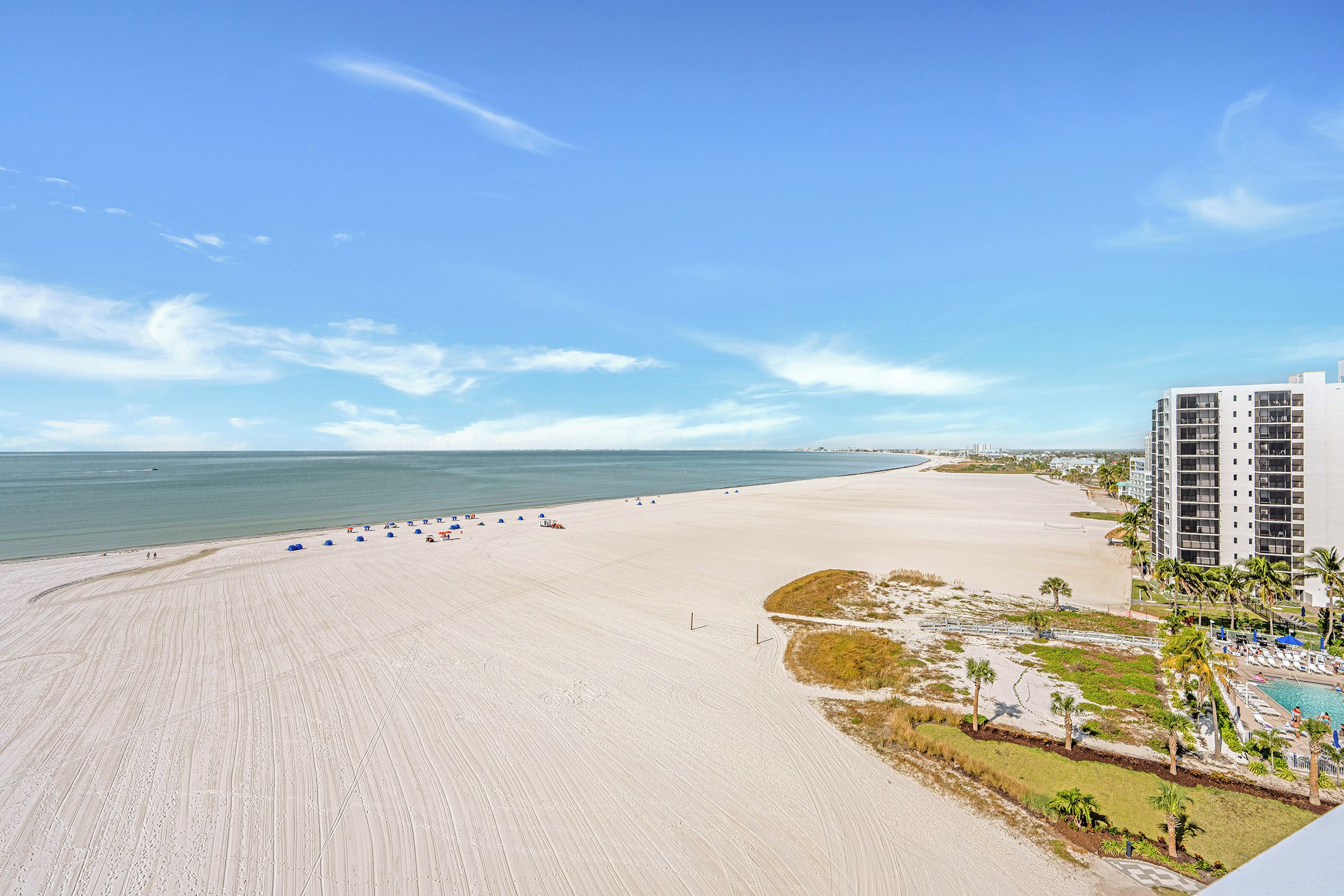 A beach with a clear sky, a sandy shore, and a hotel building with multiple floors.