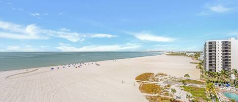 A beach with a clear sky, a sandy shore, and a hotel building with multiple floors.