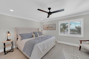 Un dormitorio con cama, mesitas de noche, ventilador de techo y una ventana con persianas.