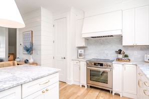A modern kitchen with white cabinetry, a built-in oven, and a marble countertop. - Relaxin @ The Roses II - Brand New Home with Amazing Sound Views (Surf City)