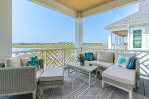 A covered outdoor seating area with wicker furniture, a small table, and a view of a bridge and water. - Relaxin @ The Roses II - Brand New Home with Amazing Sound Views (Surf City)