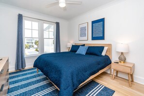 A bedroom with a bed, two bedside tables, a nightstand, a window with curtains, and artwork on the wall. - Relaxin @ The Roses II - Brand New Home with Amazing Sound Views (Surf City)