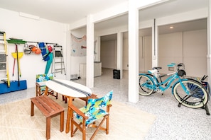A room with a dining table, chairs, a surfboard, and a bicycle. - Relaxin @ The Roses II - Brand New Home with Amazing Sound Views (Surf City)