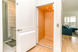 A room with a wooden floor, a white door, and a view of a balcony with a sofa. - Relaxin @ The Roses II - Brand New Home with Amazing Sound Views (Surf City)