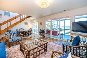 A spacious living area with a glass coffee table, wicker furniture, a television, and a view of the outdoors. - Faded Blue - 3 BR Soundfront Home in Channelbend (Surf City)
