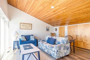 A room with two sofas, a table, and a chair. There are wooden doors and a ceiling with wooden slats. - Faded Blue - 3 BR Soundfront Home in Channelbend (Surf City)