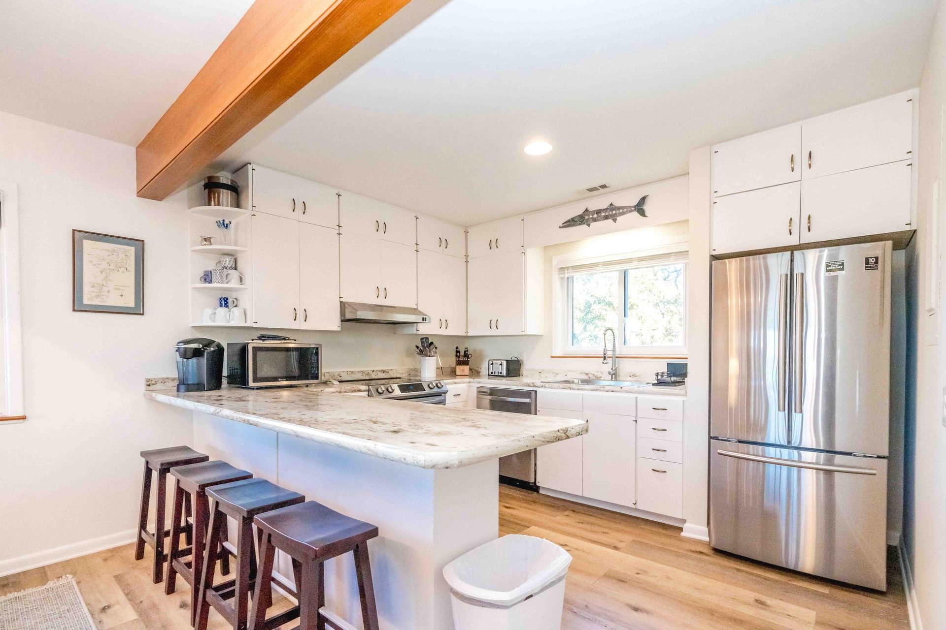A modern kitchen with white cabinetry, a stainless steel refrigerator, a built-in oven, and a large island with bar stools.