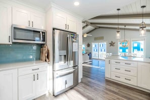 A modern kitchen with white cabinetry, stainless steel appliances, and a view to a beach house. - Loggerhead Landing - Spacious 5BR Home with Cov. Porches & Ocean Views (Surf City)