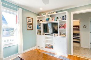 Un salon avec un téléviseur, des étagères à livres et des tableaux encadrés accrochés au mur.