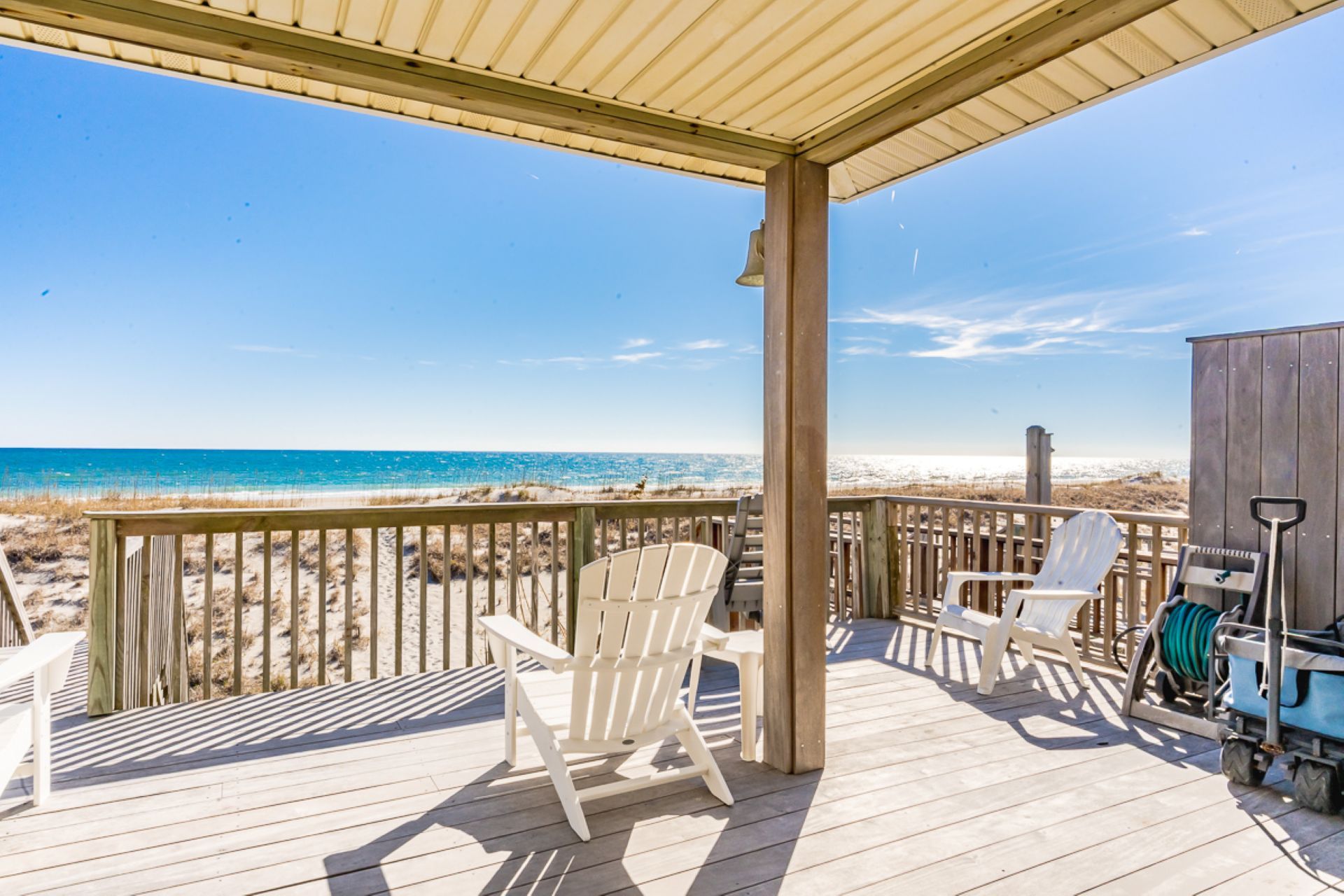 A wooden deck with white chairs overlooking a beach.