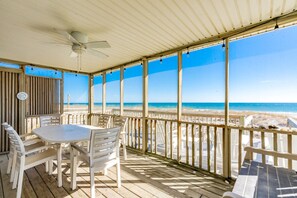 A covered outdoor area with a table and chairs, overlooking a beach. - Good Company - Classic 3BR Oceanfront Beach Cottage with Screen Porch (Topsail Beach)
