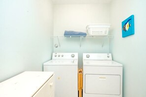 Une buanderie équipée de deux machines à laver, d’un sèche-linge, d’une étagère avec un panier et d’un tableau accroché au mur.