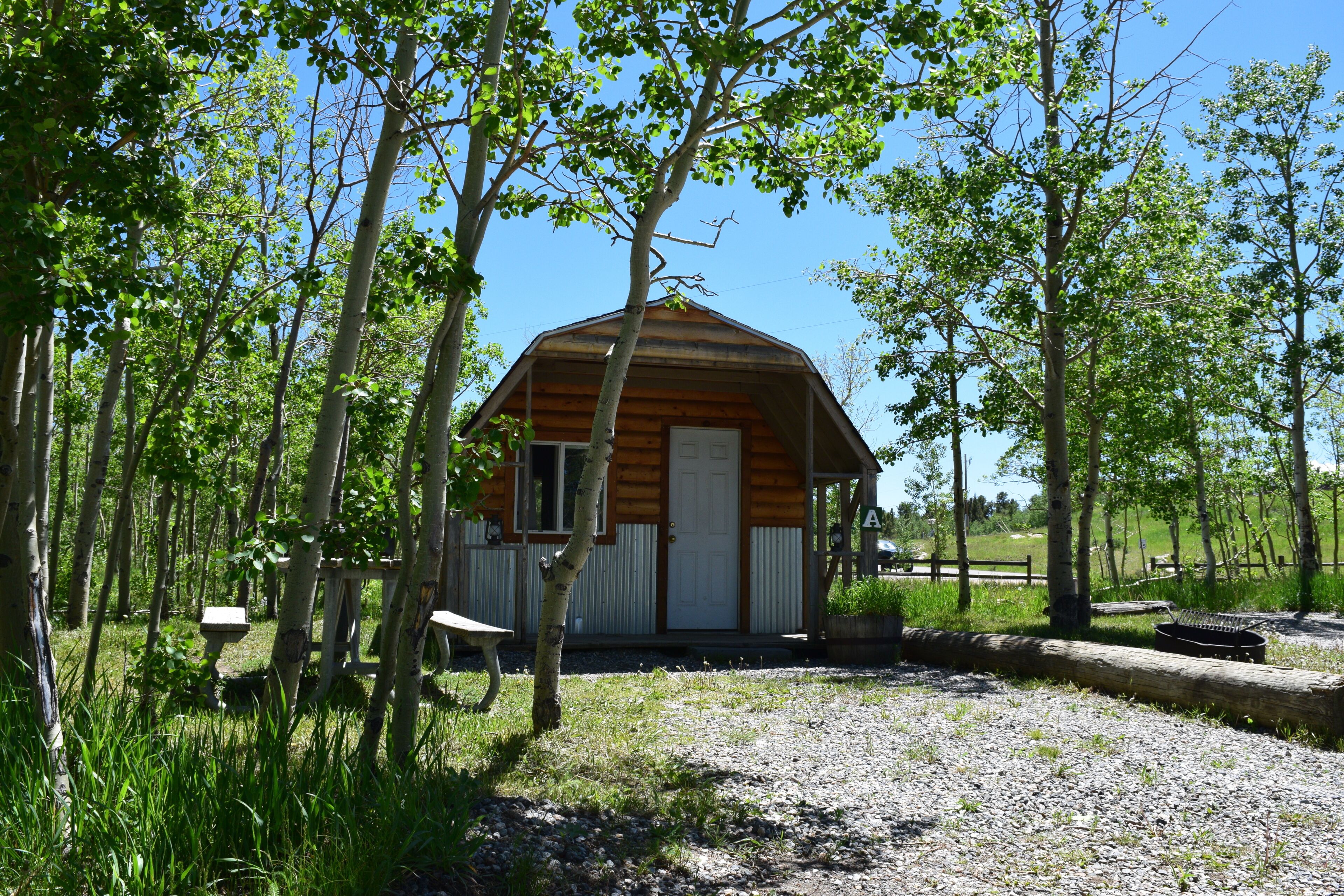 A small wooden cabin with a pitched roof, surrounded by trees and a gravel path.