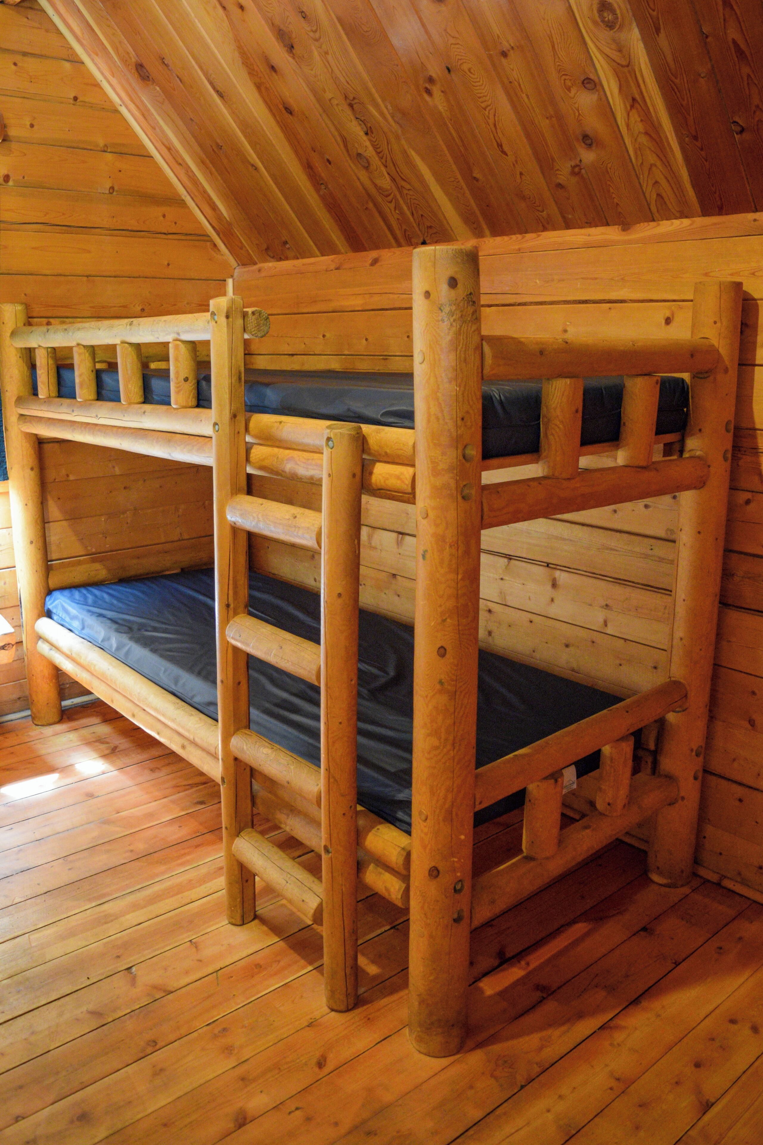 Una cama individual superpuesta con escalera, paredes de madera y techo inclinado.