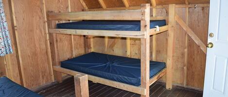 Een stapelbed met houten frame en blauwe matrasbeschermers in een kamer met houten wanden en een schuin dak.