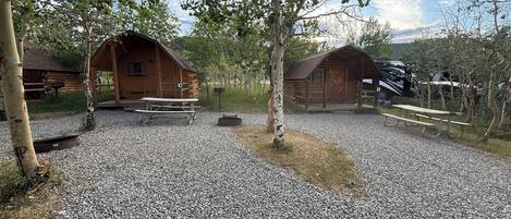 A rustic cabin area with wooden cabins, picnic tables, and gravel paths.