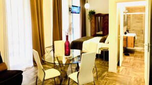 Camera d'albergo con zona pranzo, televisore, divano e bagno visibile attraverso una porta aperta.