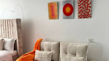 Een moderne woonkamer met een beige bank, een kamerkleed met dessin en drie abstracte schilderijen aan de muur.