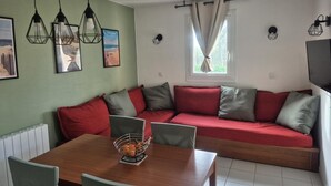 Un salon chaleureux avec une table à manger en bois, un canapé rouge agrémenté de coussins gris et un téléviseur fixé au mur.