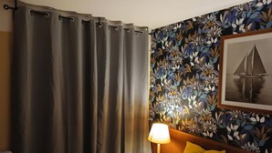 Une chambre d’hôtel avec un lit, une table de chevet avec une lampe, un rideau et un papier peint à motifs floraux.
