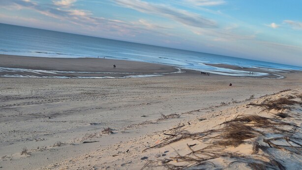 Une plage avec une vaste étendue de sable, quelques personnes dispersées le long du rivage et l’océan en arrière-plan.