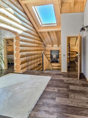 A log cabin interior with a skylight, wooden staircase, and a view into another room.