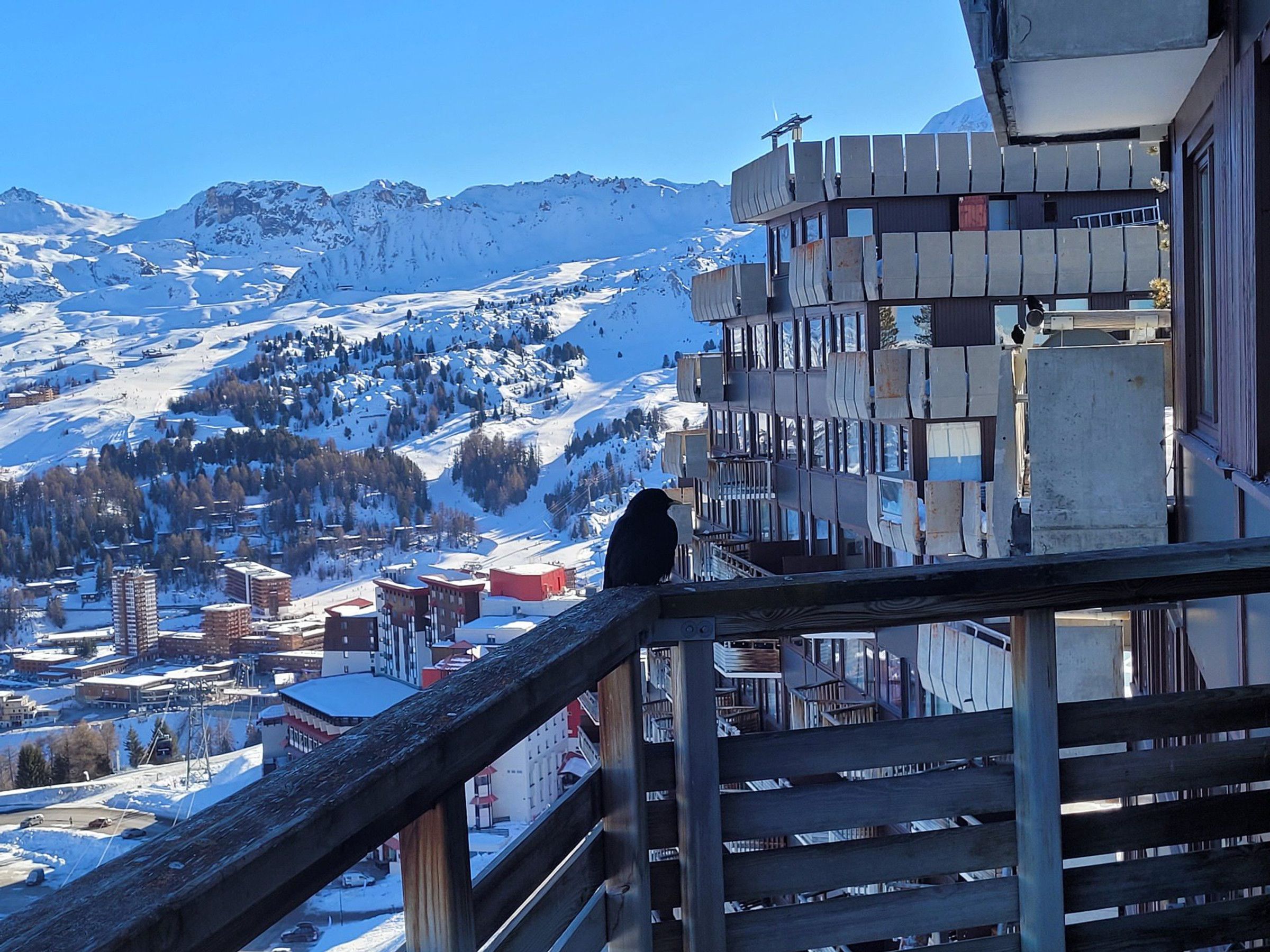 A person on a balcony overlooking a snowy mountain landscape with buildings in the foreground.
