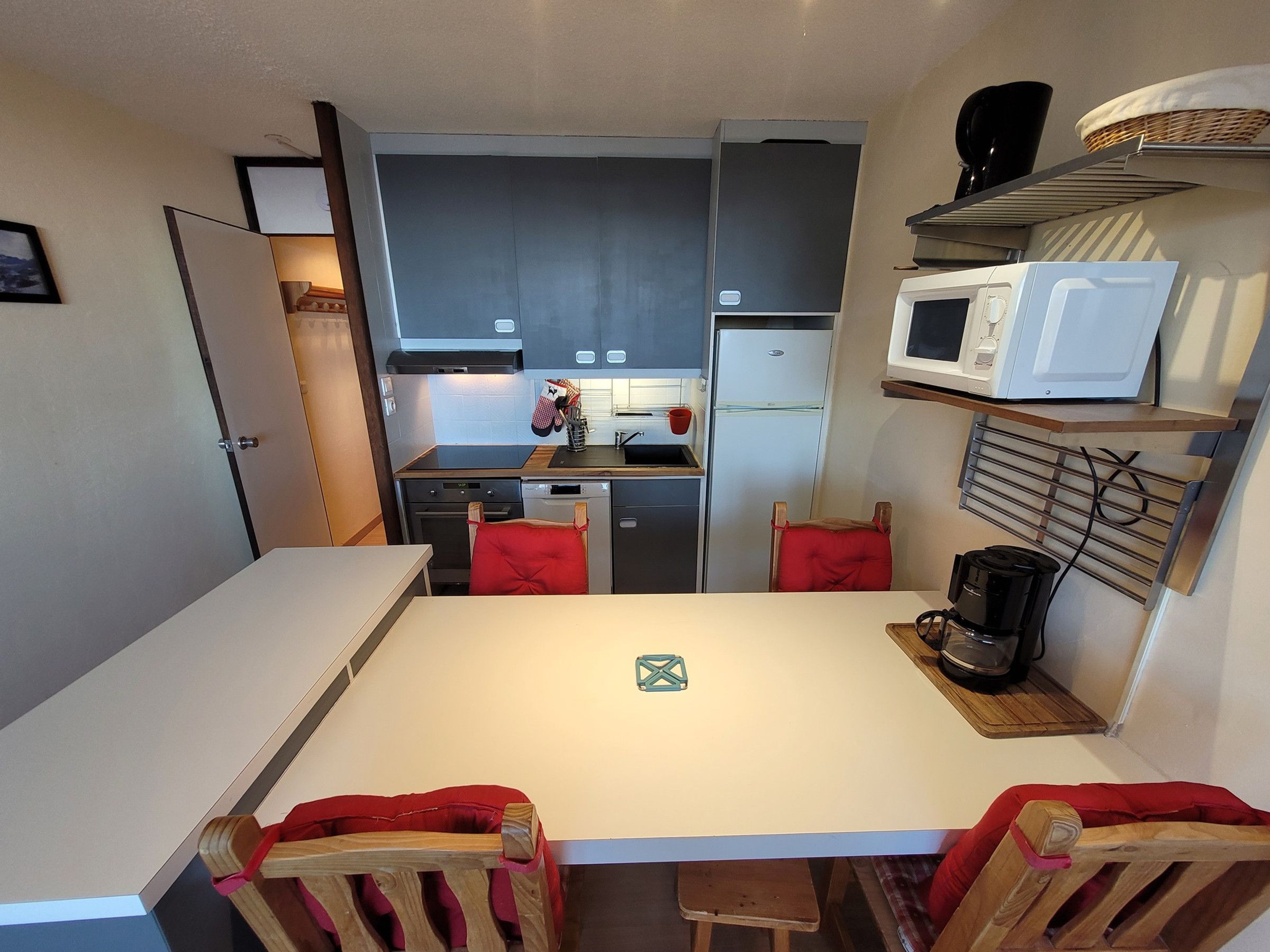 Una cocina compacta con encimera blanca, microondas, cafetera y una silla roja.