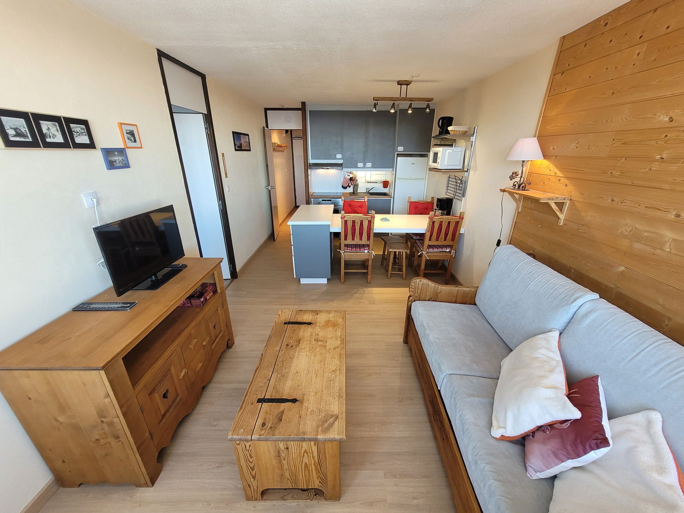 Ett kompakt vardagsrum med en soffa, ett träbord, en TV, ett litet kök och en matplats.