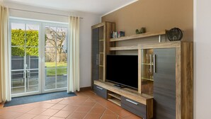 Una sala de estar moderna con un televisor de pantalla plana grande, estanterías de madera y un ventanal corredero que da a un espacio exterior.