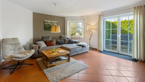 Una sala de estar con un sofá, un sillón, una mesa de centro y un ventanal con cortinas.