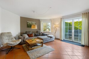 Una sala de estar con un sofá, un sillón, una mesa de centro y un ventanal con cortinas.