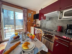 A kitchen with a dining table set for breakfast, including croissants, fruits, and a coffee maker. - Cozy apartment near slopes and shops with terrace (Vars)