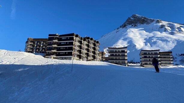 Ein mit Schnee bedeckter Berg, im Hintergrund moderne, mehrstöckige Gebäude.
