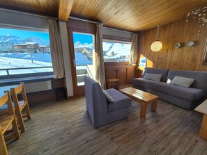 A cozy room with a wooden ceiling, a grey sofa, a small wooden table, and a view of a snowy mountain. - Functional ski-in/ski-out apartment with balcony in Tignes (Tignes)