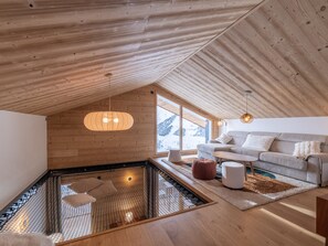 A modern interior with a sloped ceiling, a seating area with a sofa and cushions, a small table, and a large window offering a view of the outdoors. - Spacious apartment for 8 people, mountain view, Wi-Fi, parking (Huez)
