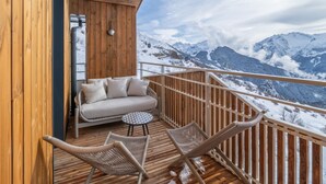 En träveranda med en soffa och två stolar, med utsikt över ett snötäckt berglandskap.