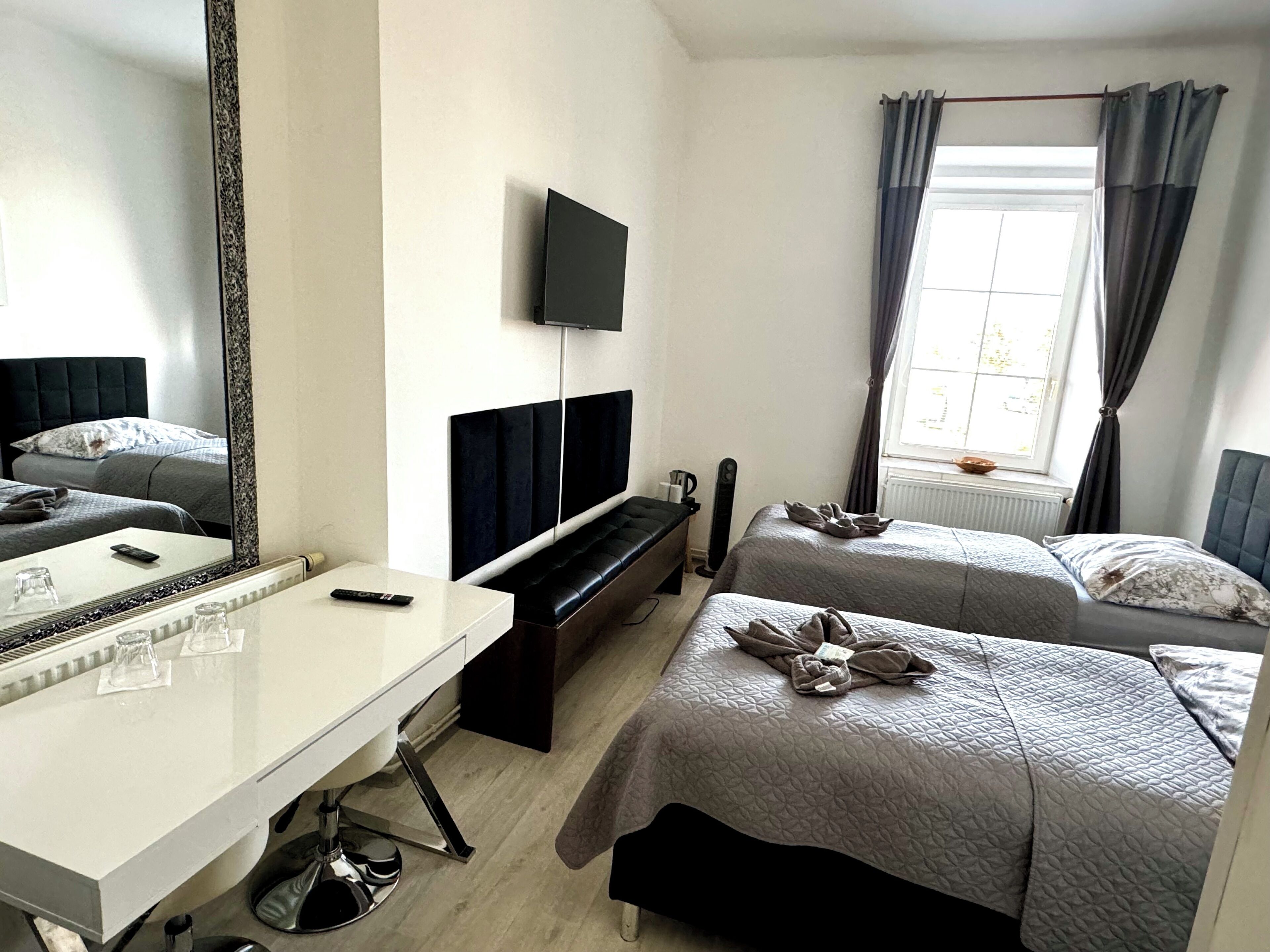 Una camera d'albergo con un letto, una scrivania, una TV e una finestra con tende.