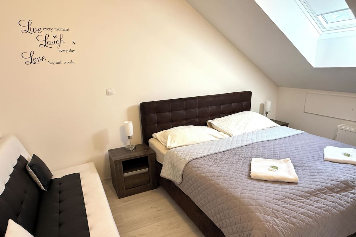 A bedroom with a large bed, a nightstand, a bedside table, and a skylight.