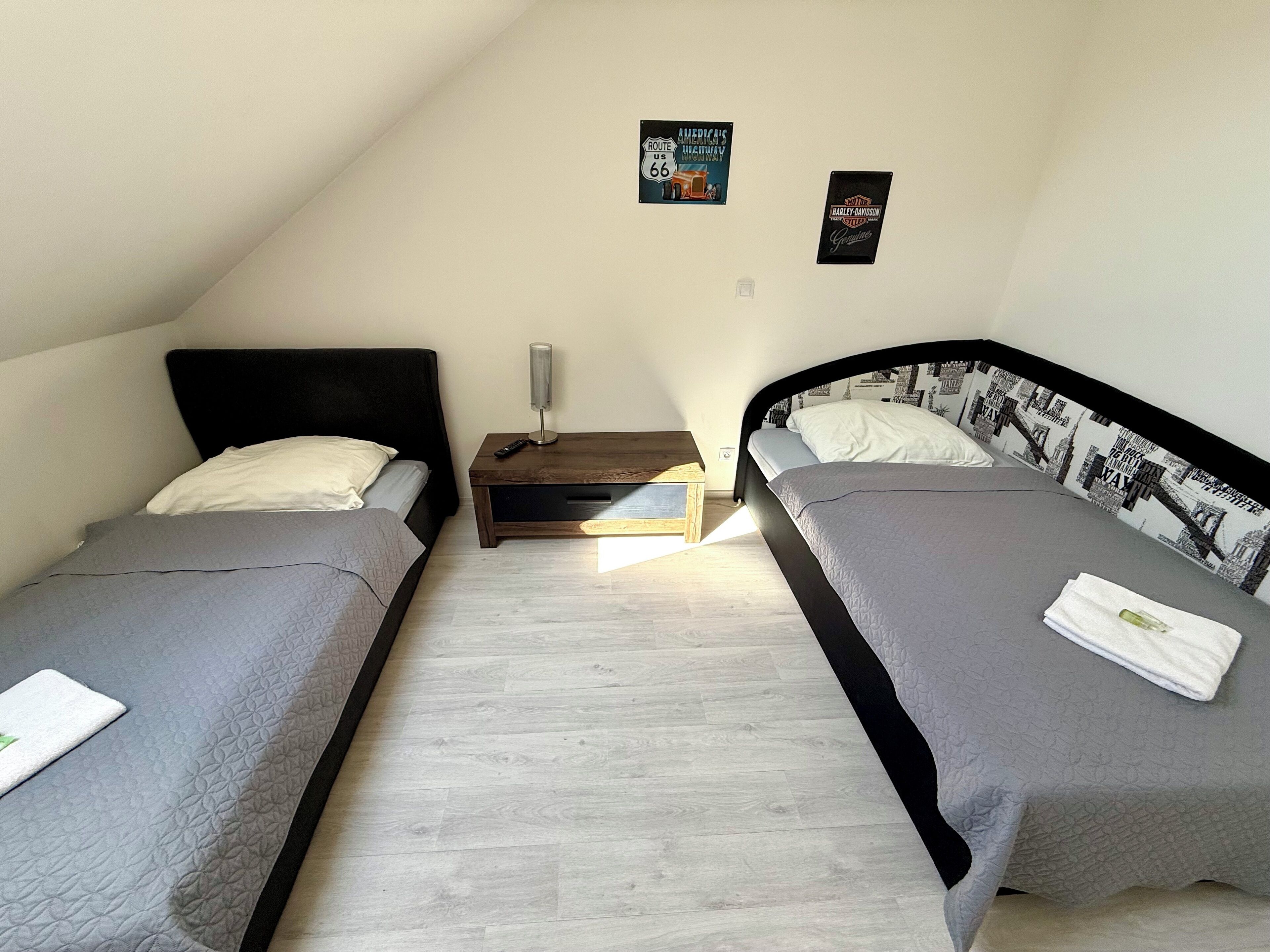 A bedroom with two single beds, a nightstand, and a wall-mounted lamp.