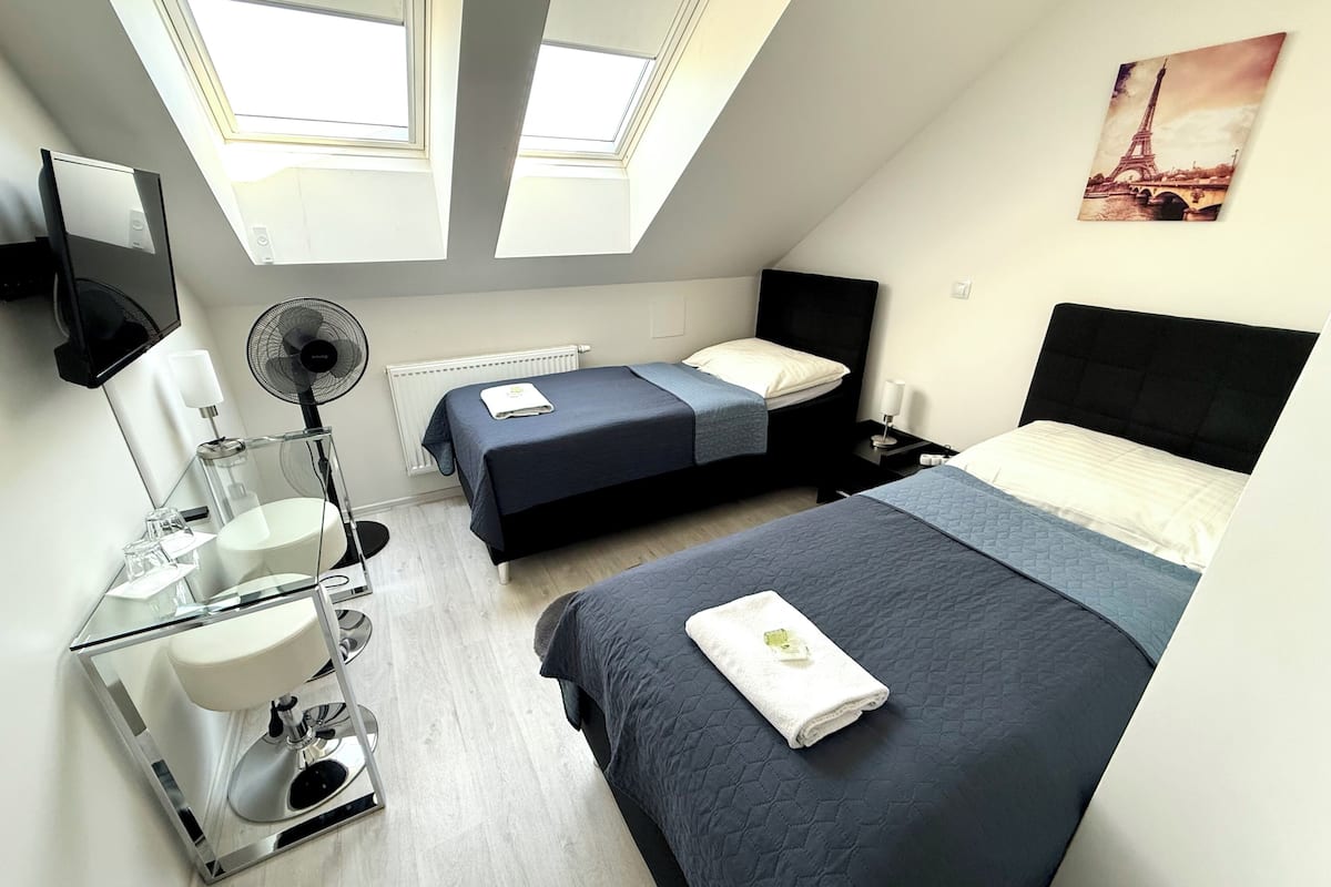 A modern hotel room with two beds, a bathroom, a skylight, and a painting of the Eiffel Tower.