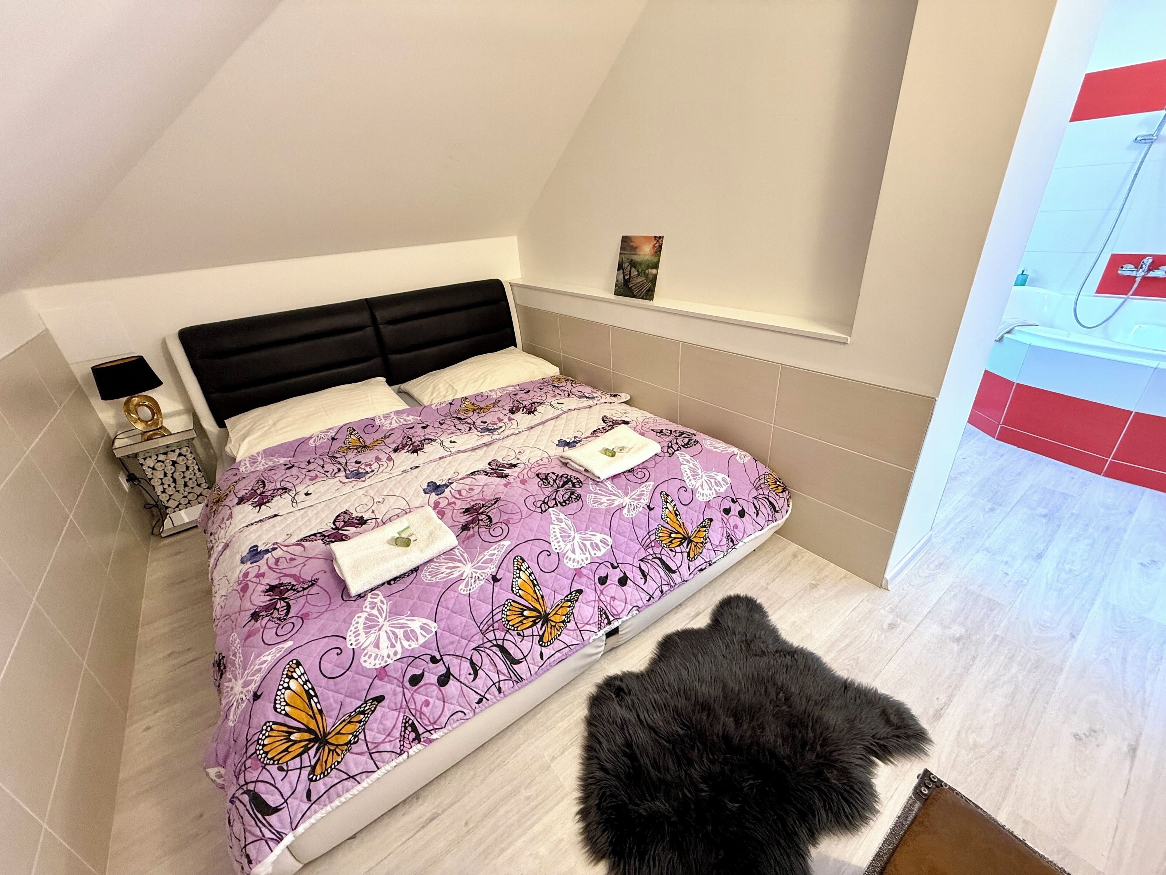 A bedroom with a bed, a nightstand, a mirror, and a black furry rug.