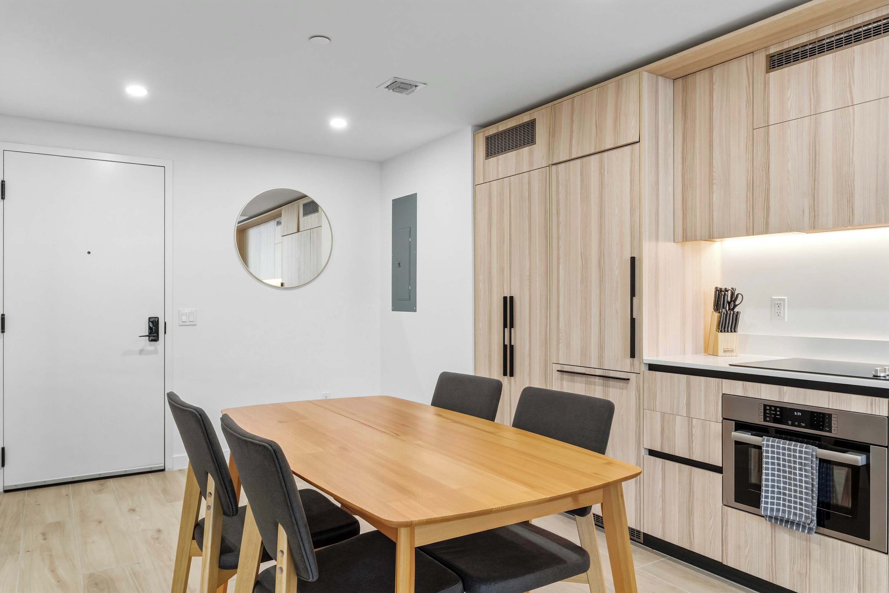 A modern kitchen with wooden cabinets, a built-in oven, and a round mirror on the wall.