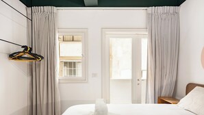 Une chambre d’hôtel avec un lit, un banc, une fenêtre et une porte.