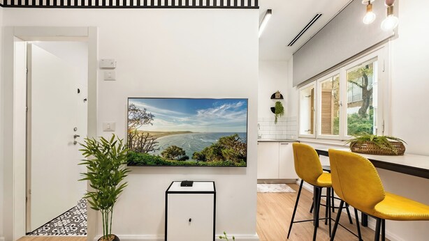 Une cuisine moderne avec une grande fenêtre, un coin repas avec des chaises jaunes et un téléviseur fixé au mur.