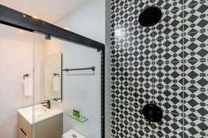Un baño moderno con cabina de ducha de vidrio, lavamanos blanco y pared con diseño.
