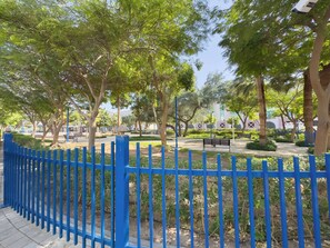 A park with a blue fence, trees, a bench, and a pathway. - Stayshort - 1 Bedroom in Al Garhoud That Sleeps 2 (Dubai)