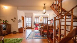 A spacious living area with a wooden staircase, a dining table with chairs, and a kitchen area. - Alonia Forest House - Limni Plastira Getaway (Lake Plastiras)